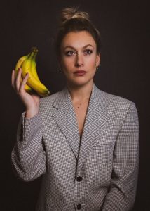 Fenella Ryan headshot, where she is holding a bunch of bananas.