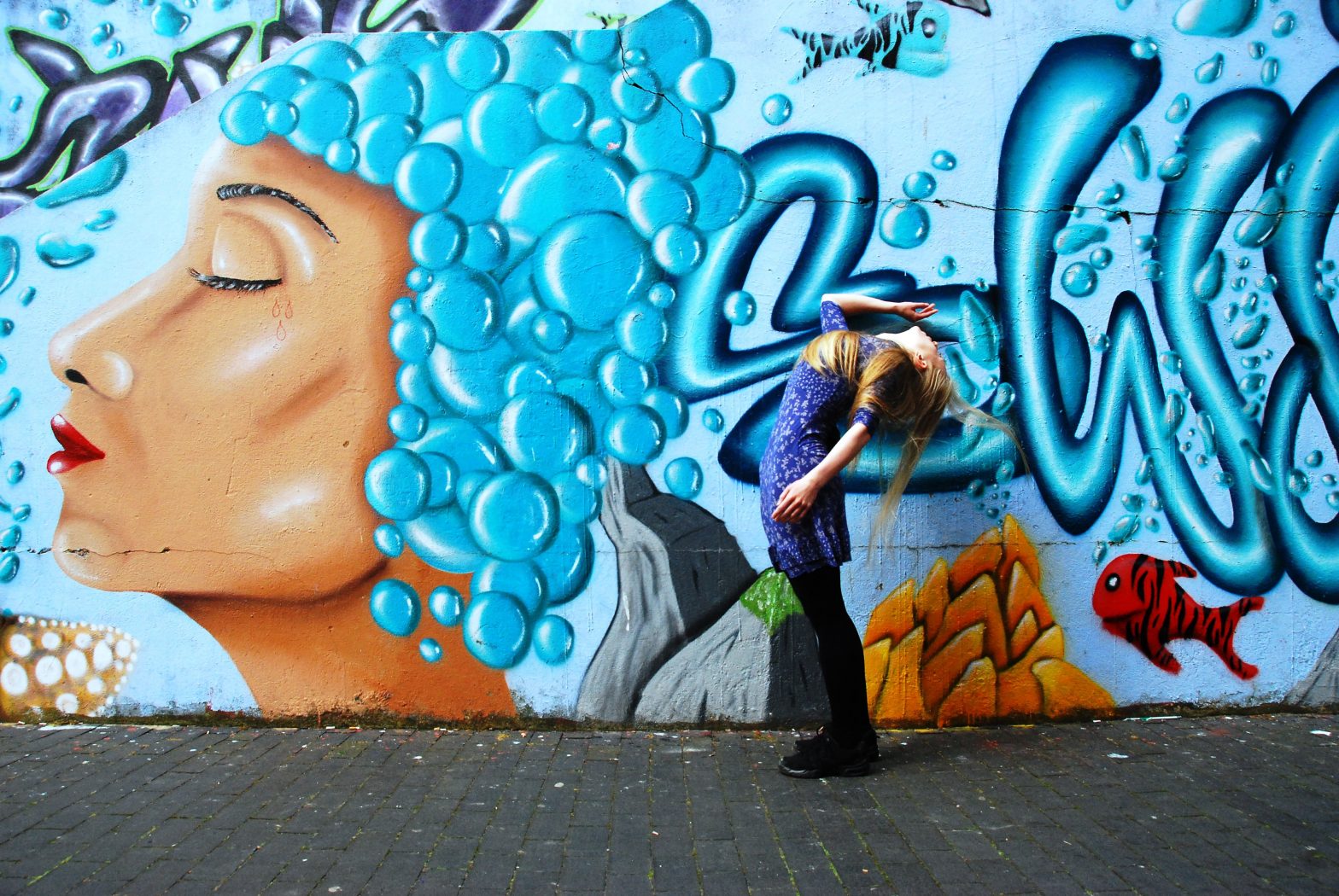 A woman leans back against a backdrop of a blue graffiti