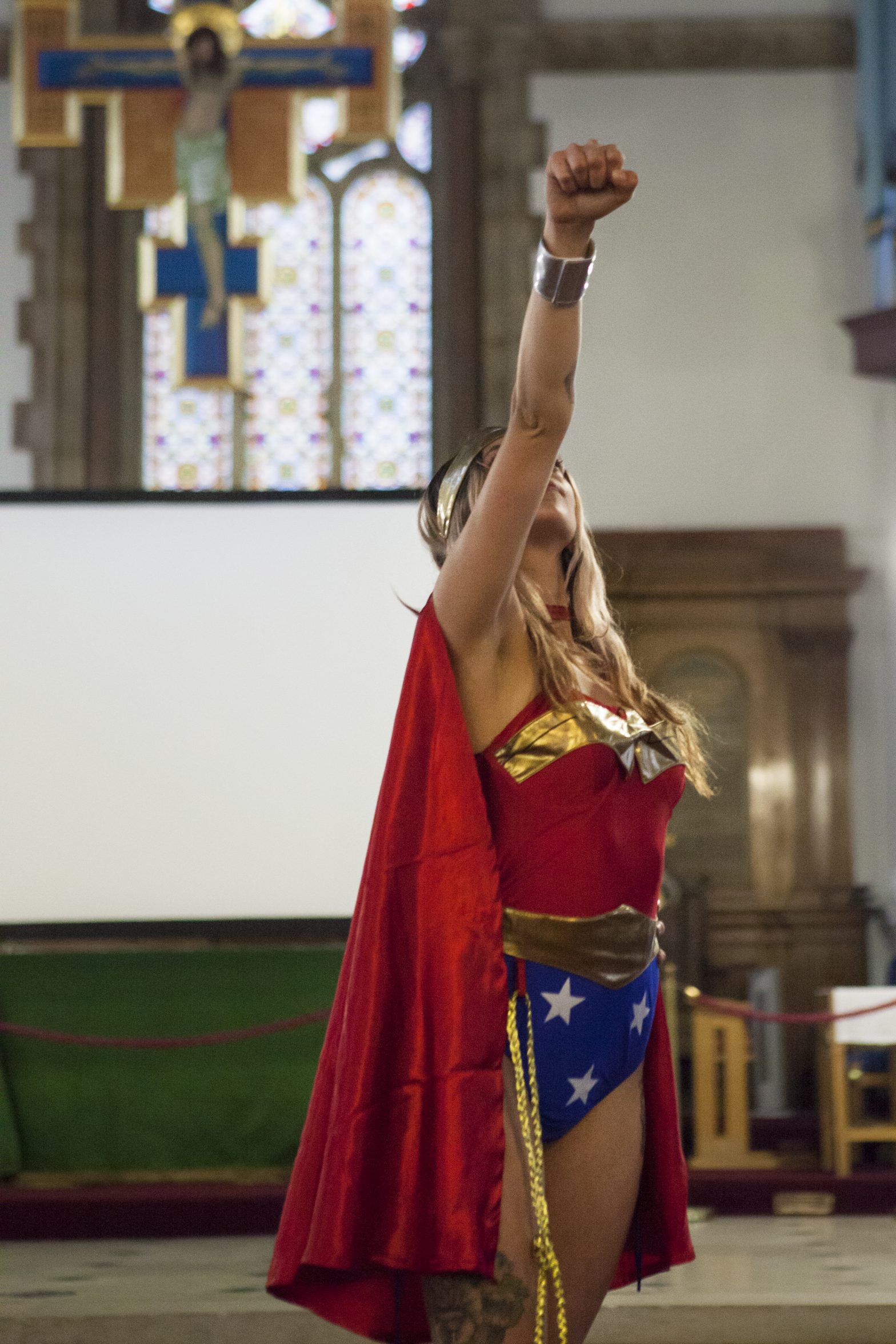 A woman is dressed as a superhero. Her arm is raised above her head.