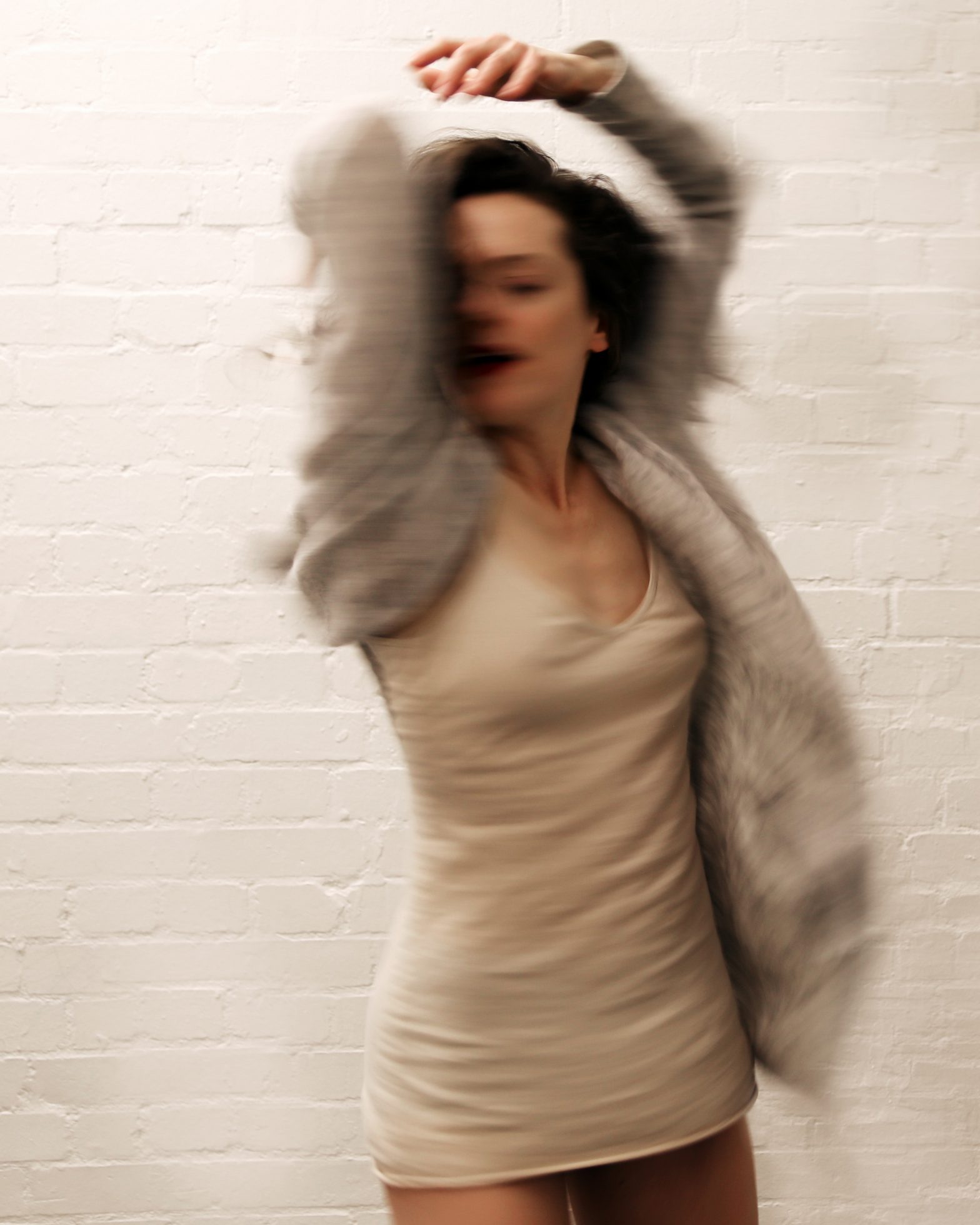Photo of Laura Careless. She is wearing a cream dress and jacket, her arms are above her head and her body is slightly twisted.
