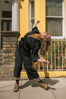 A women dances in front of a yellow wall on the street.