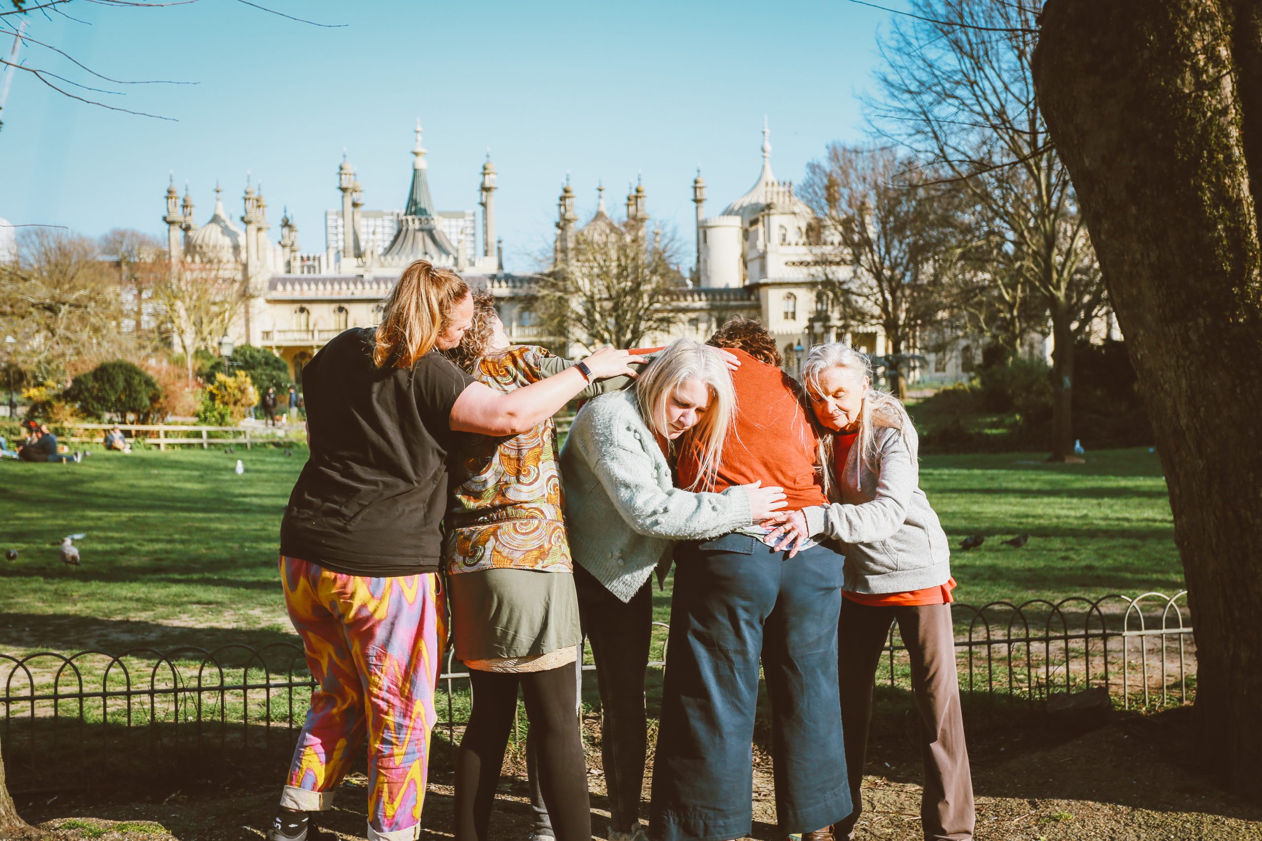 A group of women hug each other in a park.