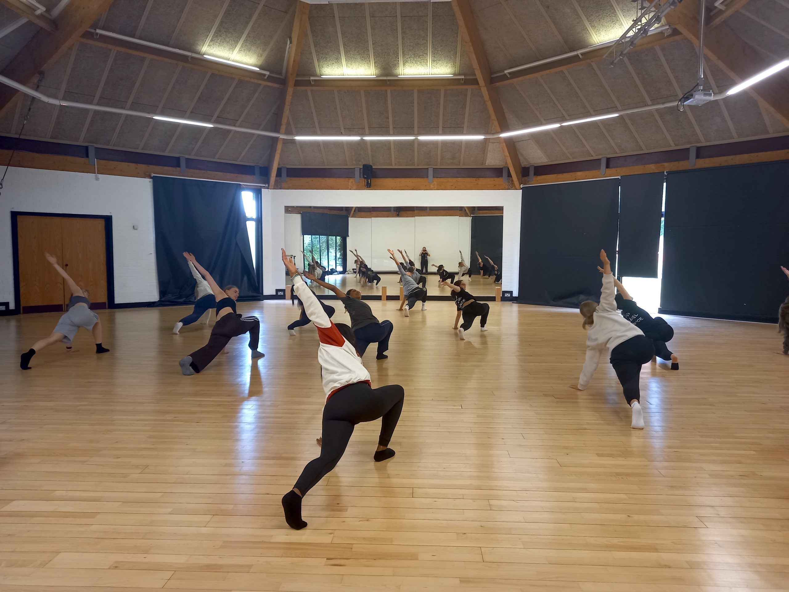 A group of dance students are dancing. They all have one hand on the floor, the other stretched above them as they lunge.