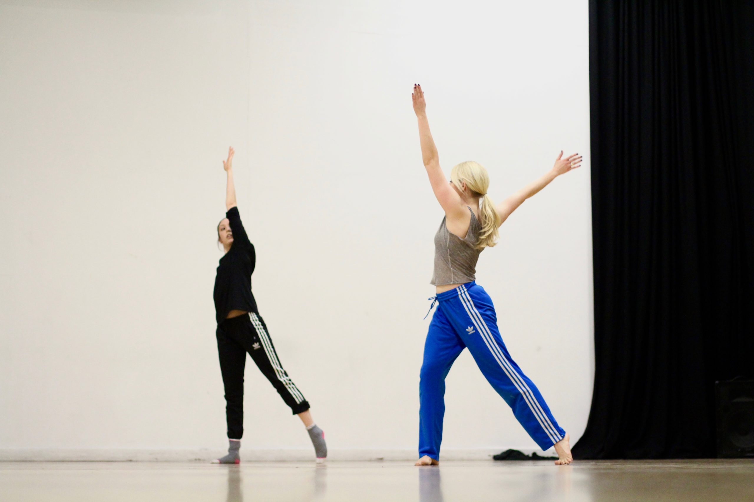 Two dancers are in a space. Arms lifted and one leg to the side.