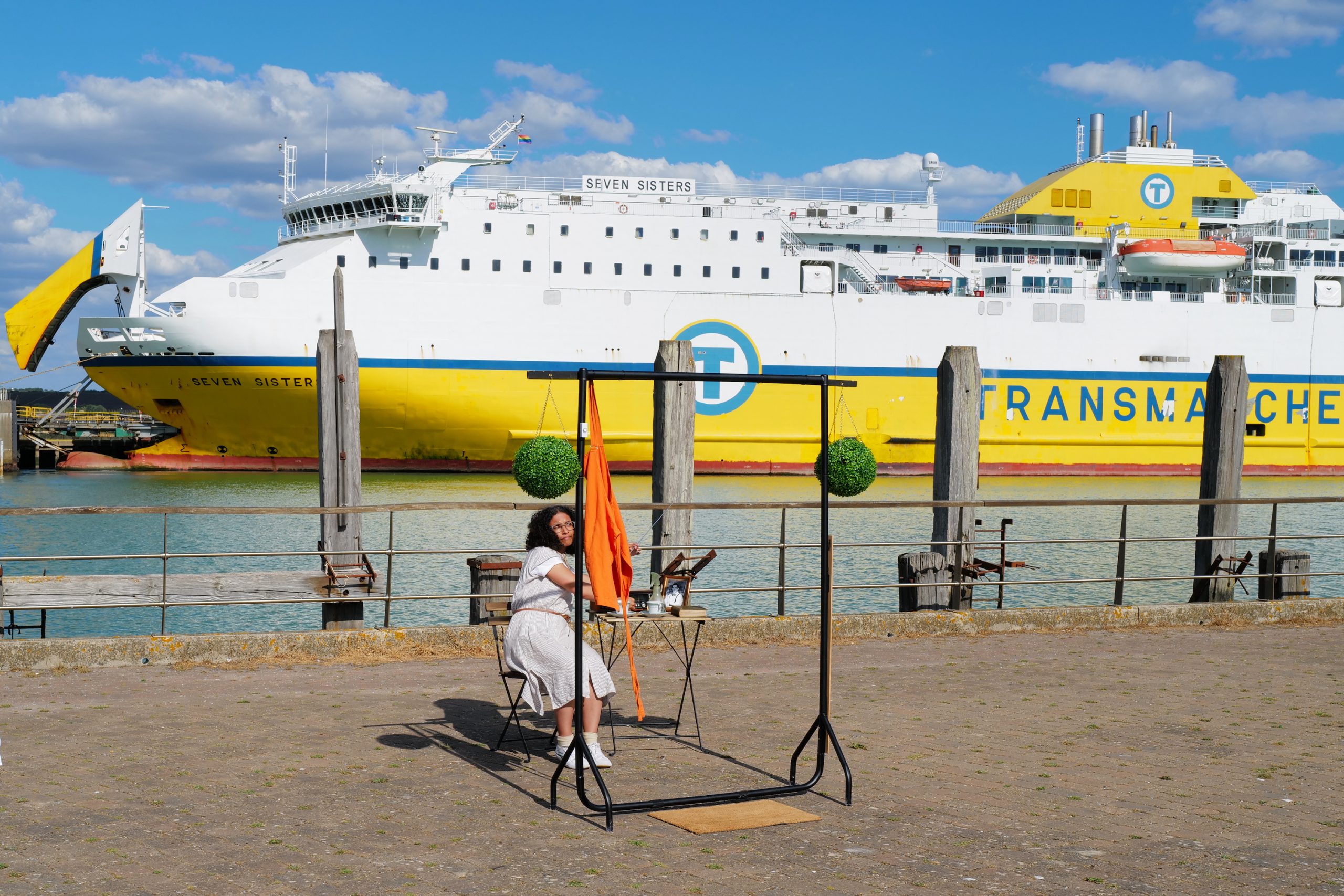A woman performs in front of a ferry. She is tuning the radio.