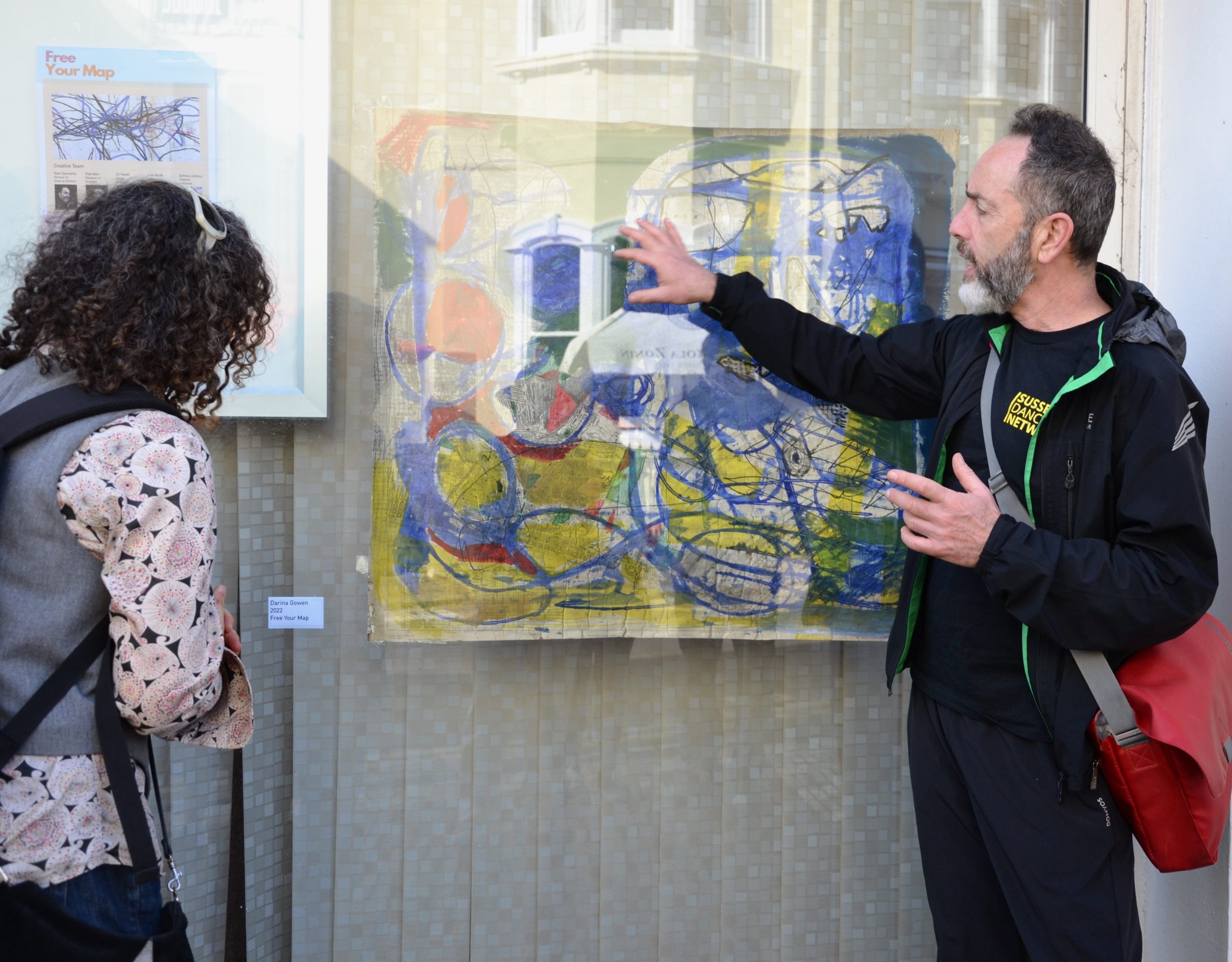 A man points at a painting displayed in a window as a woman looks at it.