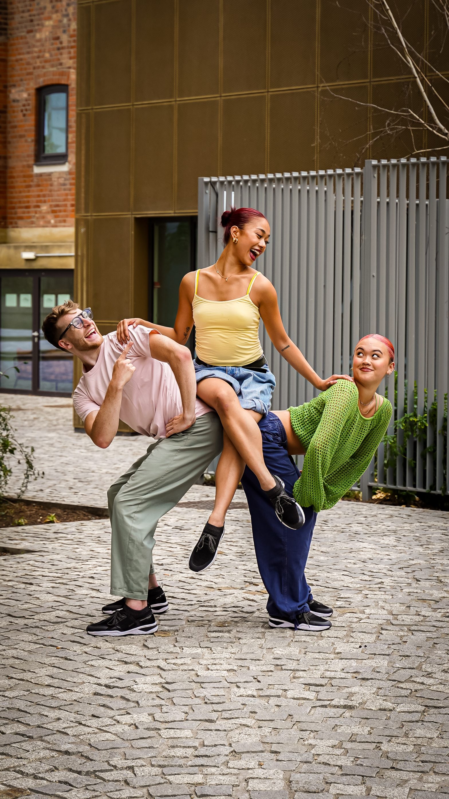 Three people dance o the street. Two are lifting one person up.
